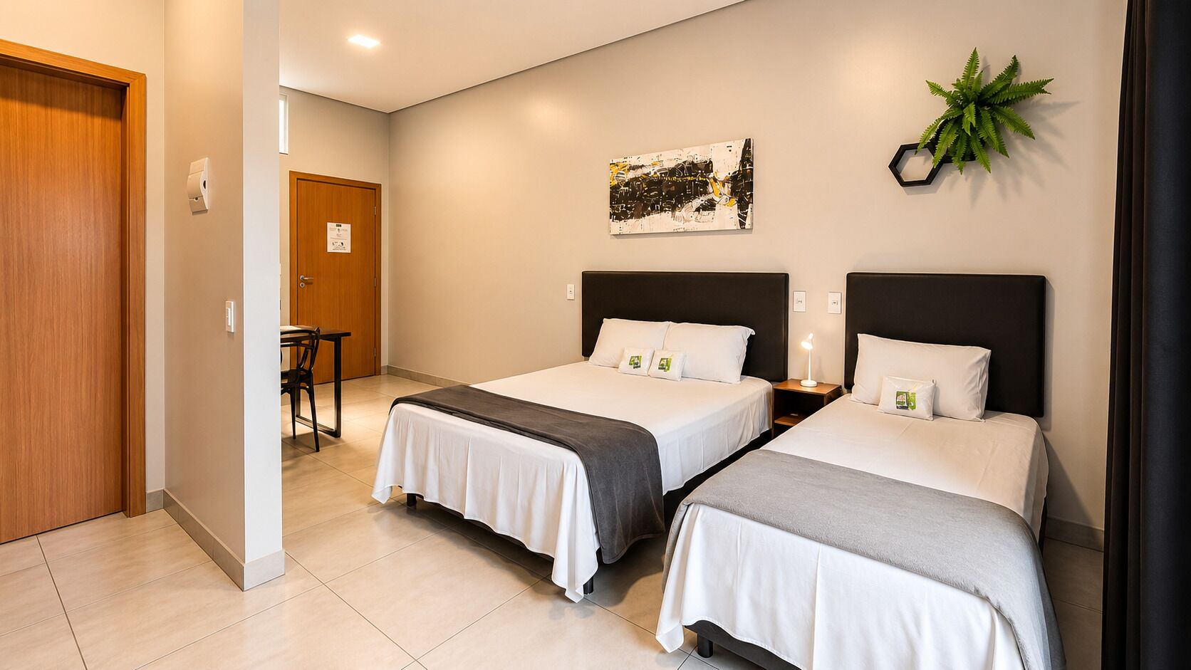 Hotelkamer met twee bedden, een bureau, een stoel, een plant en een schilderij aan de muur.