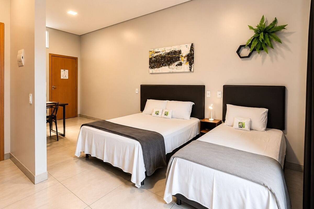 A hotel room with two beds, a desk, a chair, a plant, and a painting on the wall.