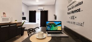 A modern hotel room with a bed, a desk with a laptop, a coffee cup, and a wall with motivational text.