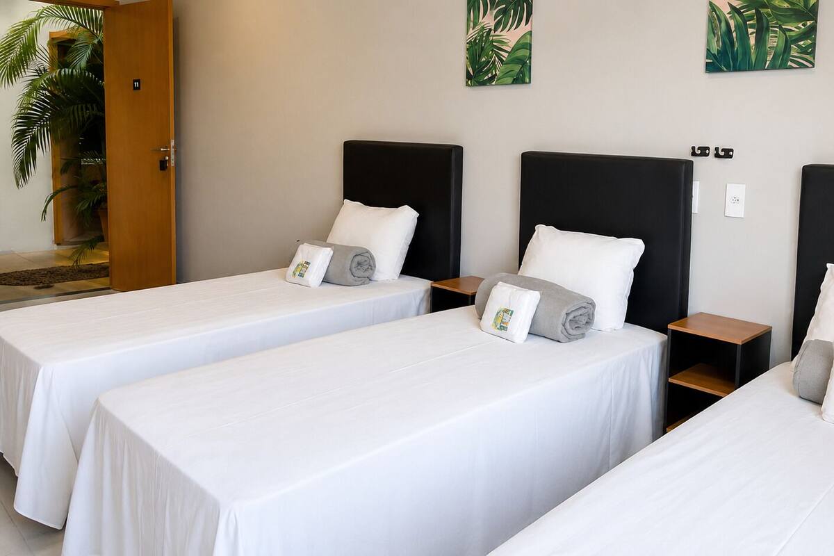 A hotel room with three single beds, each with a black headboard, white bedding, and a small wooden nightstand.