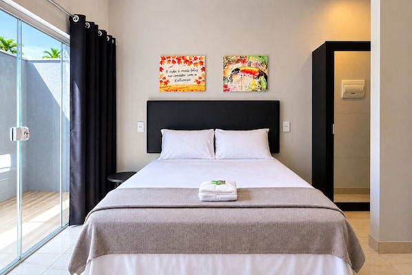 A hotel room with a bed, two wall art pieces, a window with curtains, and a door to the bathroom.