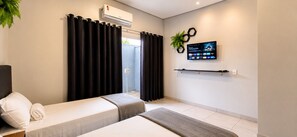 Habitación de hotel con cama, una mesita, televisor montado en la pared y ventana con cortinas.