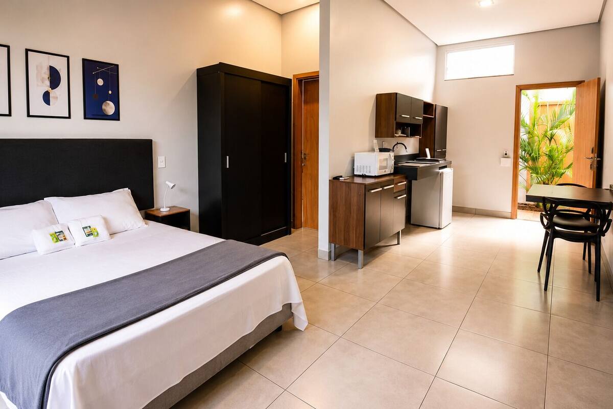 A hotel room with a bed, a desk, a kitchenette, and a dining area.