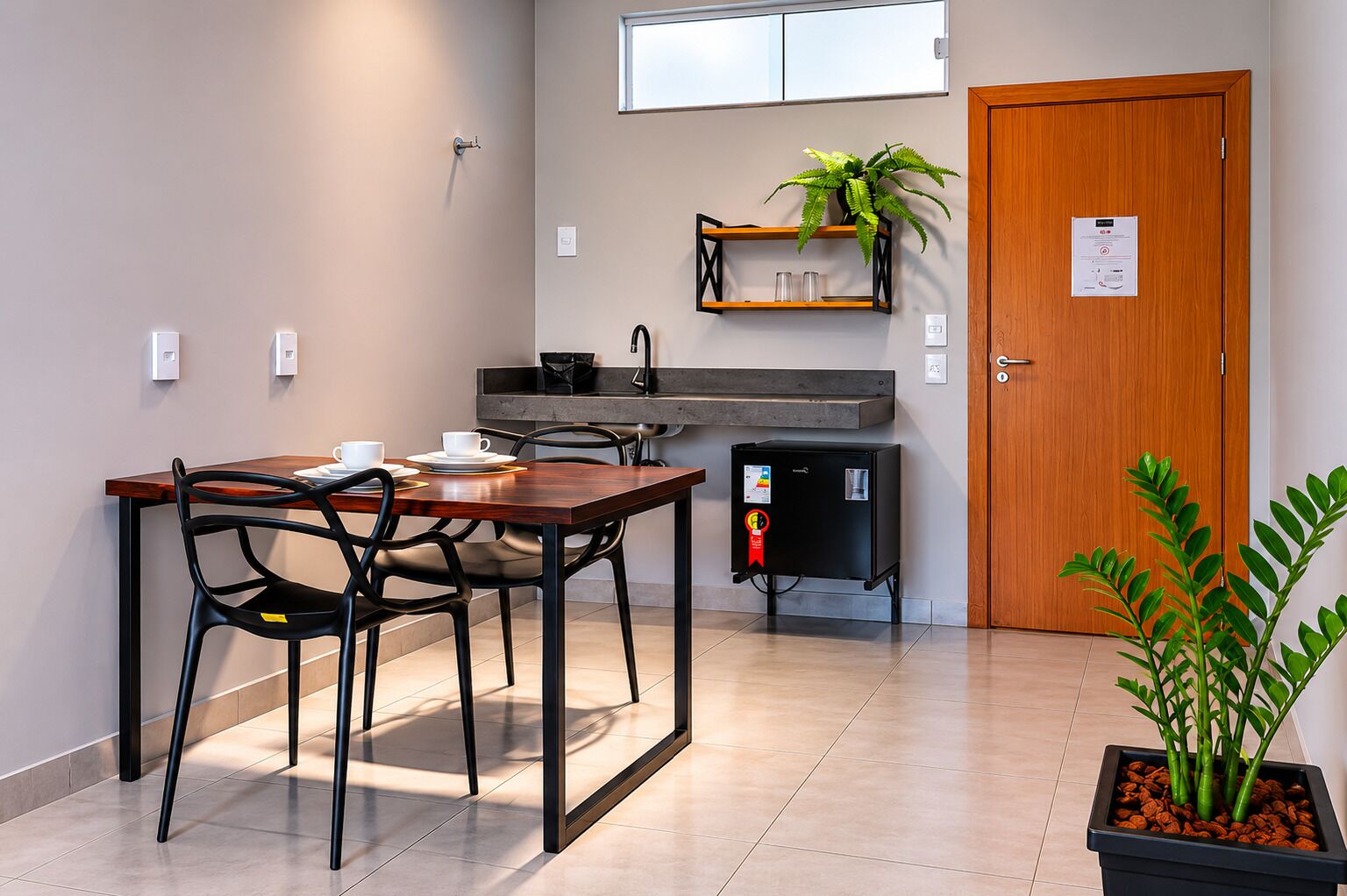 A compact kitchen with a dining table, chairs, a refrigerator, a plant, and a wooden door.