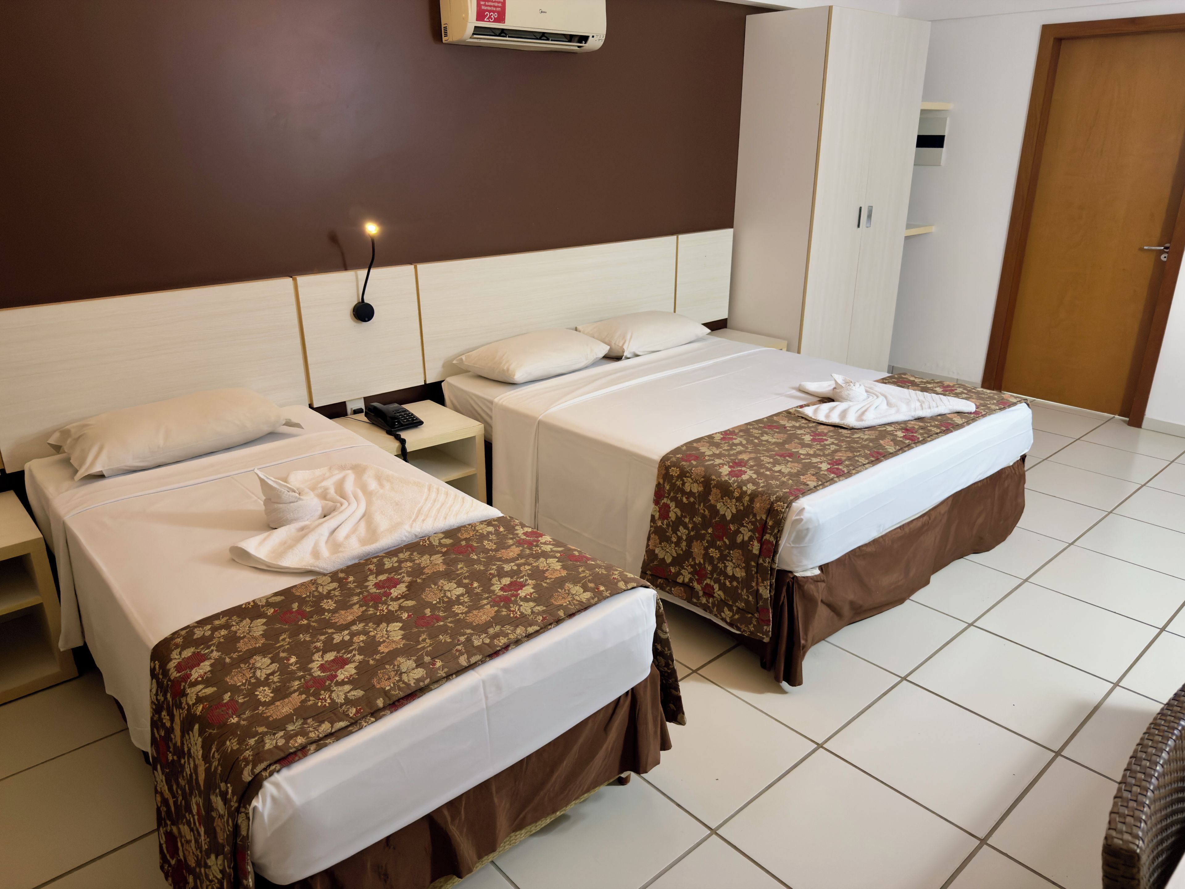 Habitación de hotel con dos camas, una mesita de noche, teléfono, armario y puerta.
