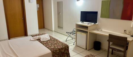 Quarto de hotel com duas camas, uma escrivaninha com computador, uma cadeira, televisão e um pequeno frigorífico.