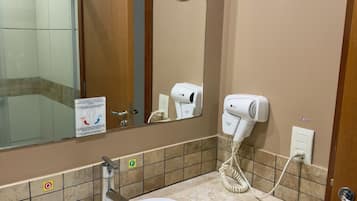Un baño con lavamanos blanco, espejo, secador de pelo y dispensador de toallas.