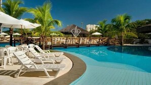 A swimming pool with lounge chairs, palm trees, and a thatched-roof structure. - Le Jardin Suites - Caldas Novas (Caldas Novas)