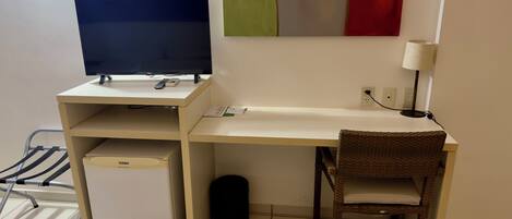 Un espacio de oficina compacto con escritorio, silla, ordenador y un refrigerador pequeño.