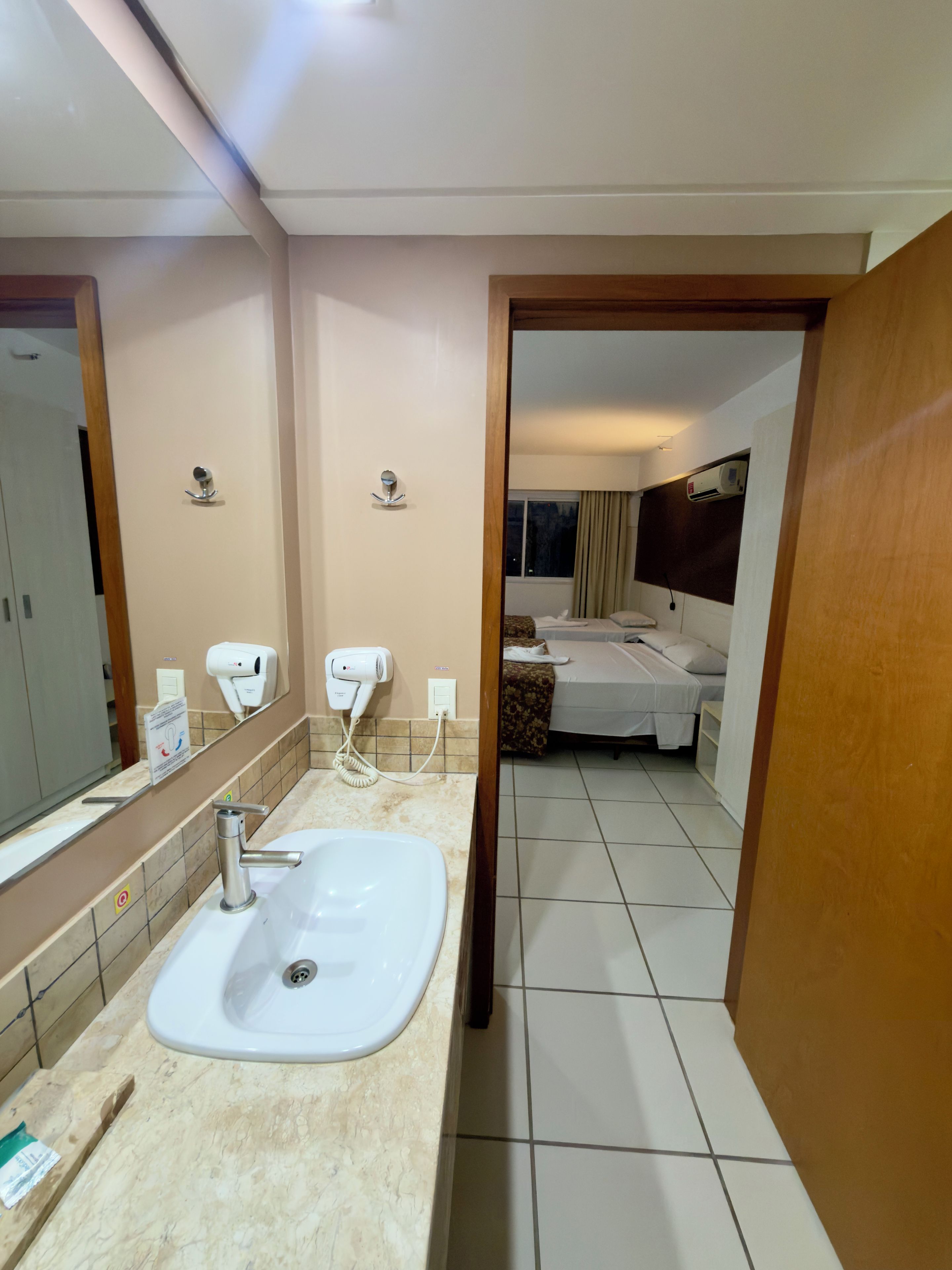 A hotel bathroom with a sink, hand dryer, and a mirror.