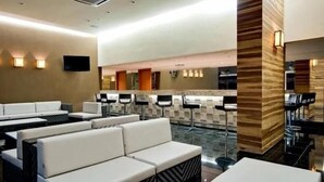 A hotel lobby with white sofas, a reception area with a counter and bar stools, and a flat-screen TV mounted on the wall. - Le Jardin Suites - Caldas Novas (Caldas Novas)