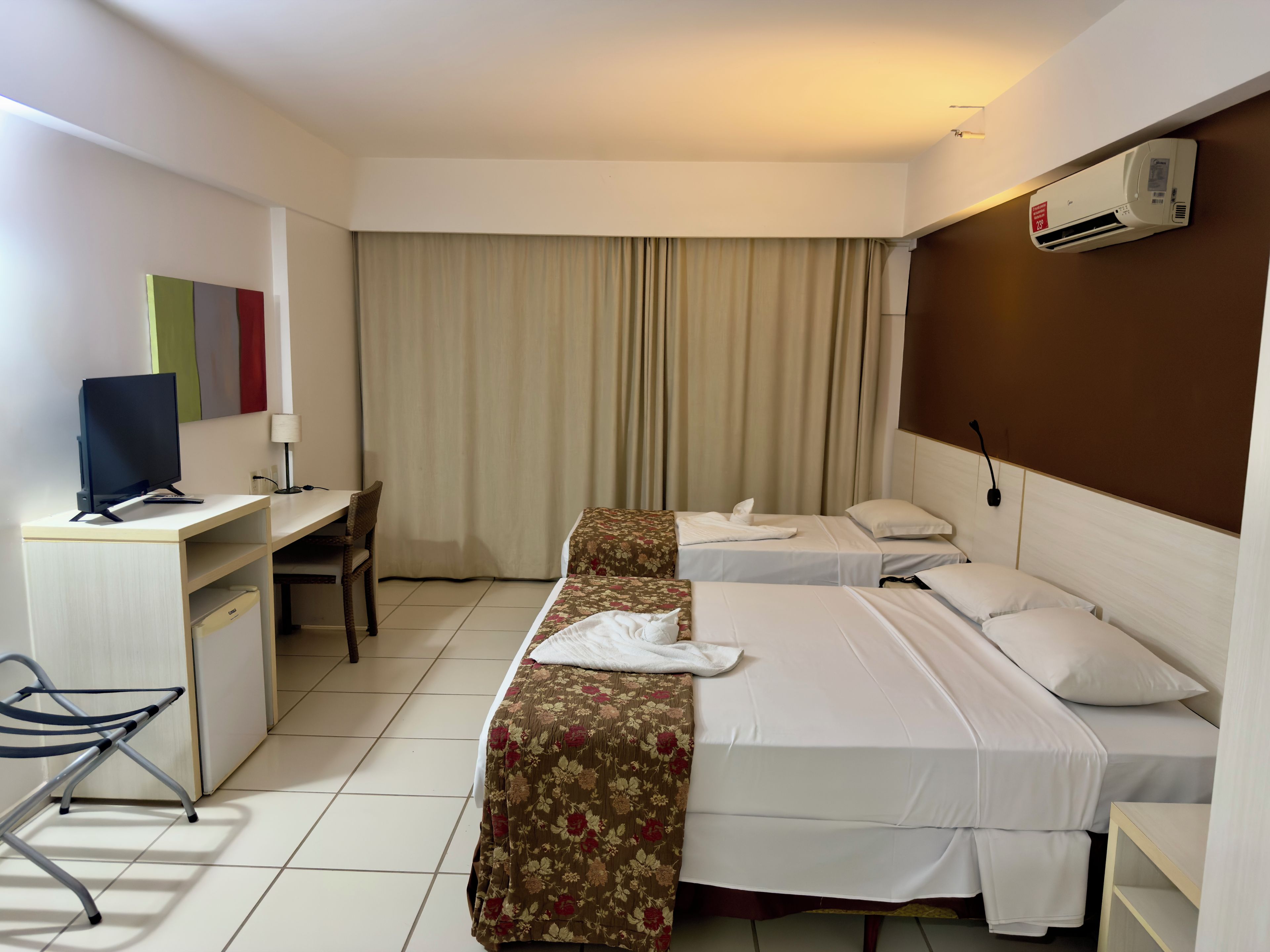Una camera d'albergo con due letti, una scrivania con un computer, una sedia e un condizionatore d'aria.
