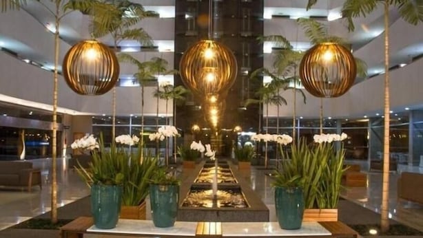 A modern lobby with a central water feature, potted plants, and hanging spherical light fixtures. - Le Jardin Suites - Caldas Novas (Caldas Novas)