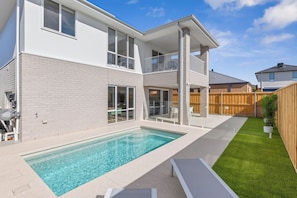 A two-story house with a swimming pool, a fenced backyard, and a wooden fence.