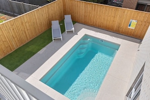 A rectangular pool with a wooden deck and two lounge chairs.
