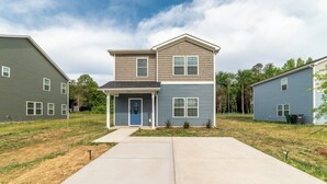 A two-story residential building with a front porch and a garage. - Brand New 3BR - Patio - Fast WiFi+Workspace - Near Airport & Whitewater Center (Charlotte)
