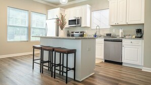 A kitchen with white cabinets, a central island with stools, a stainless steel dishwasher, and a microwave. - Brand New 3BR - Patio - Fast WiFi+Workspace - Near Airport & Whitewater Center (Charlotte)