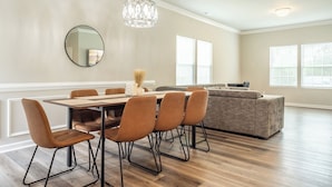 A dining area with a wooden table and chairs, a chandelier, a round mirror, and a sofa in a modern living room. - Brand New 3BR - Patio - Fast WiFi+Workspace - Near Airport & Whitewater Center (Charlotte)