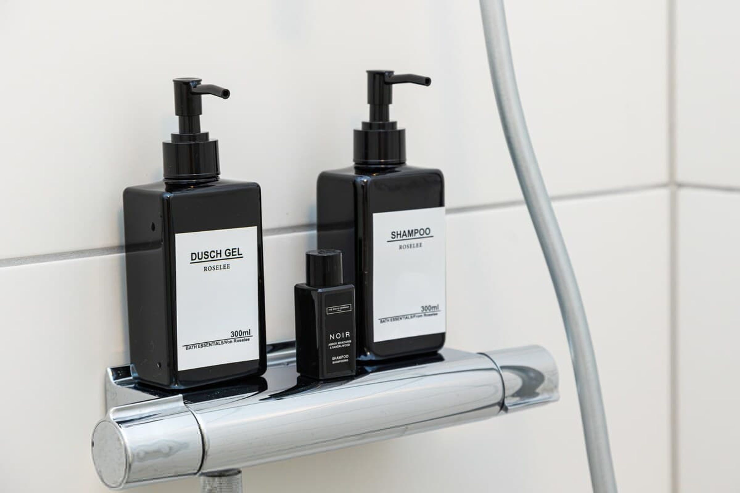 Zwei schwarze Duschgel- und Noir-Shampooflaschen auf einem Metallregal.
