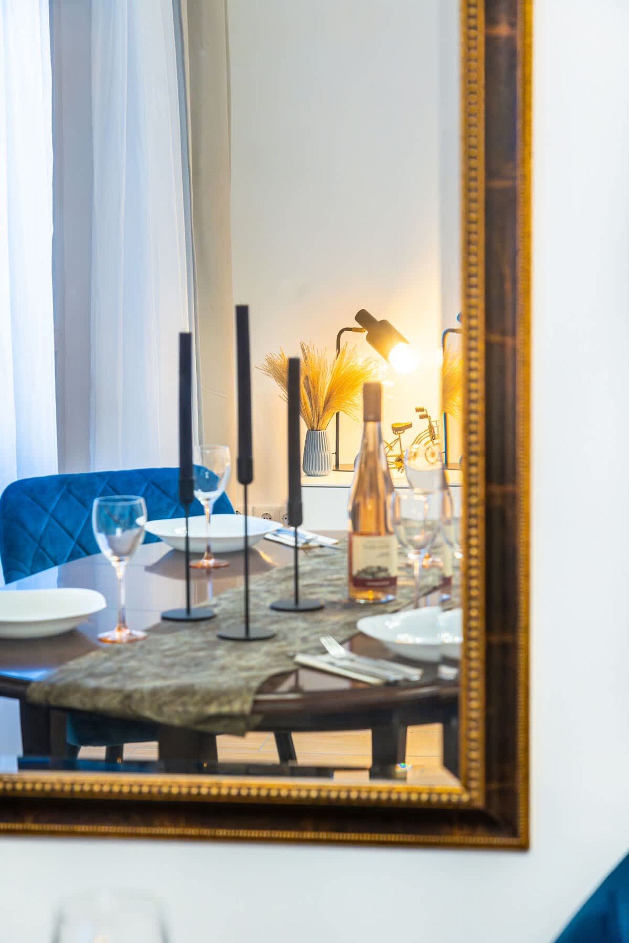 A dining table with candles, glasses, and a bottle, set against a blue chair and a mirror.