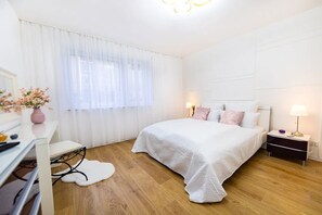 A bedroom with a bed, bedside tables, a desk, a chair, a window with curtains, and a wall-mounted light fixture. - Charmante Wohnung in Koblenz (Koblenz)