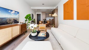 A modern living room with a flat-screen TV, a sofa, a coffee table with books, a dining area, and a kitchen. - The Pembridge Residences Building (London)