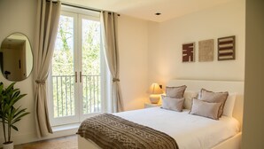 A bedroom with a bed, curtains, a bedside lamp, a mirror, and a potted plant. - The Pembridge Residences Building (London)