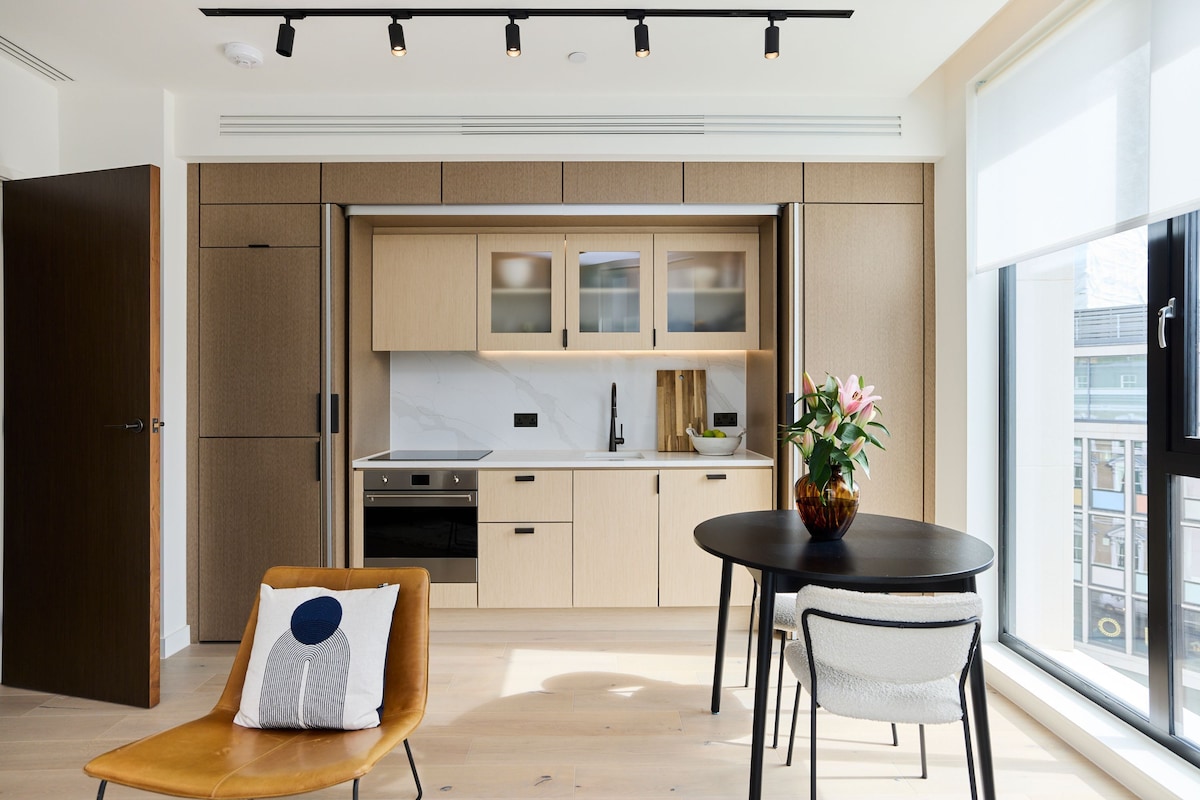 A modern kitchen with built-in appliances, a dining area with a table and chairs, and a large window offering a view.