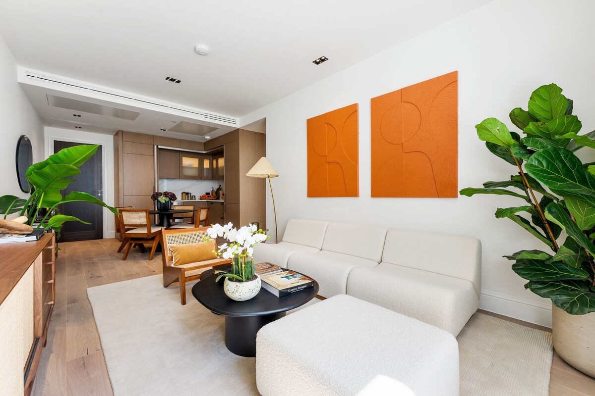 A modern living room with a sofa, coffee table, and chairs, a dining area with a table and chairs, and a kitchen in the background.