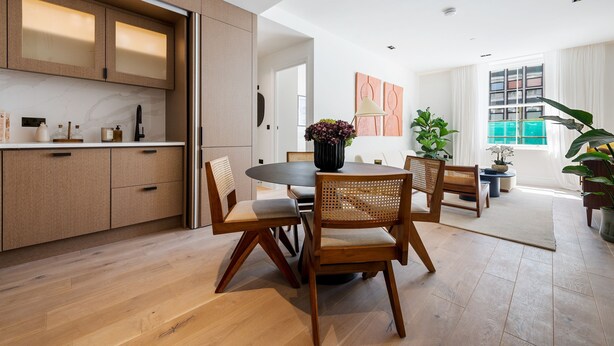 A modern kitchen with wooden cabinets, a dining area with a round table and chairs, and a view of the living room with a large window. - The Pembridge Residences Building (London)