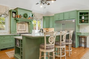Una cocina con armarios verdes, una isla central, taburetes de bar y un refrigerador.