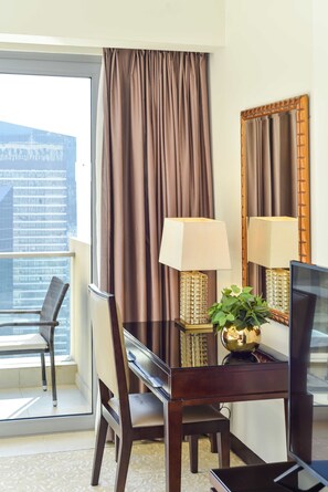 Ein Hotelzimmer mit Balkon, einem Esstisch mit Stühlen, einem Fernseher, einer Lampe und einem Spiegel.