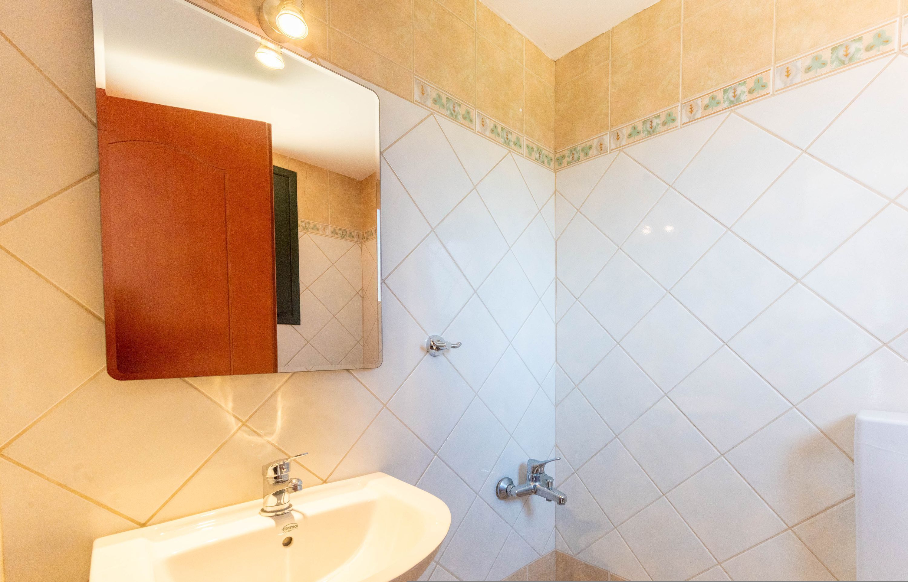 Een badkamer met een witte wastafel, een spiegel en een douchehoek.