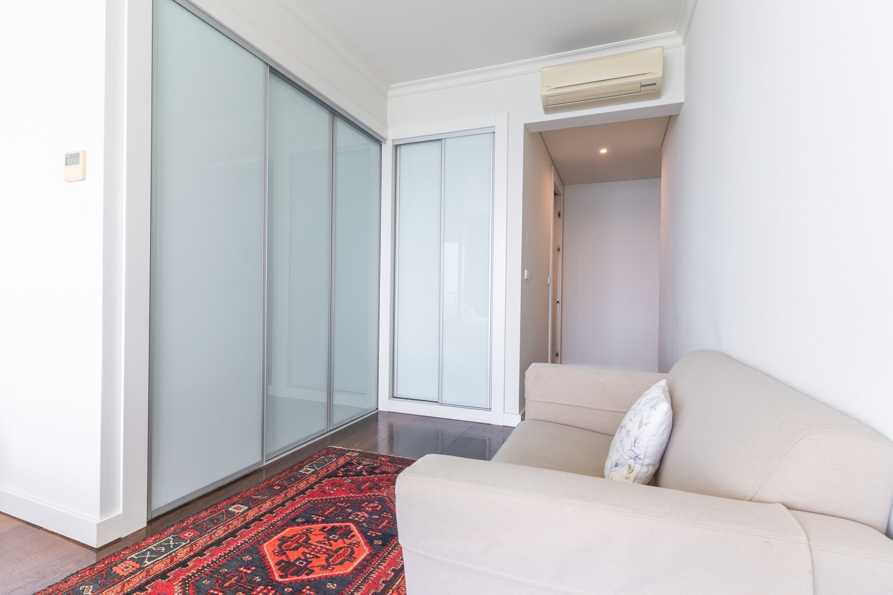 Un interior moderno con puerta corredera de vidrio, un sofá color beige y una alfombra estampada.
