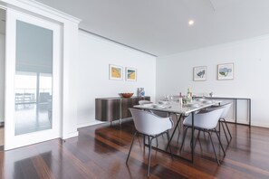 Een moderne eetruimte met een glazen deur naar een balkon, een gedekte eettafel met stoelen en kunstwerken aan de muren.