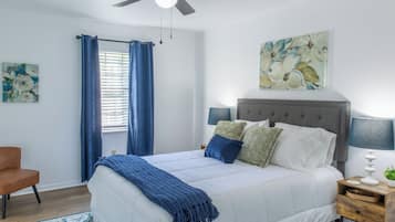 A bedroom with a bed, a nightstand, a chair, a ceiling fan, and a window with curtains.