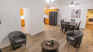 Ein modernes Wohnzimmer mit Essbereich, zwei Ledersessel, einem runden Couchtisch und einem Deckenventilator.