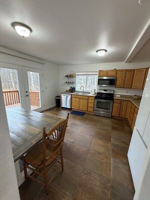 A kitchen with wooden cabinets, a stainless steel oven, a microwave, and a dining area with a table and chairs. -  3-bedroom house in charming Wasilla perfect for a family getaway (Wasilla)