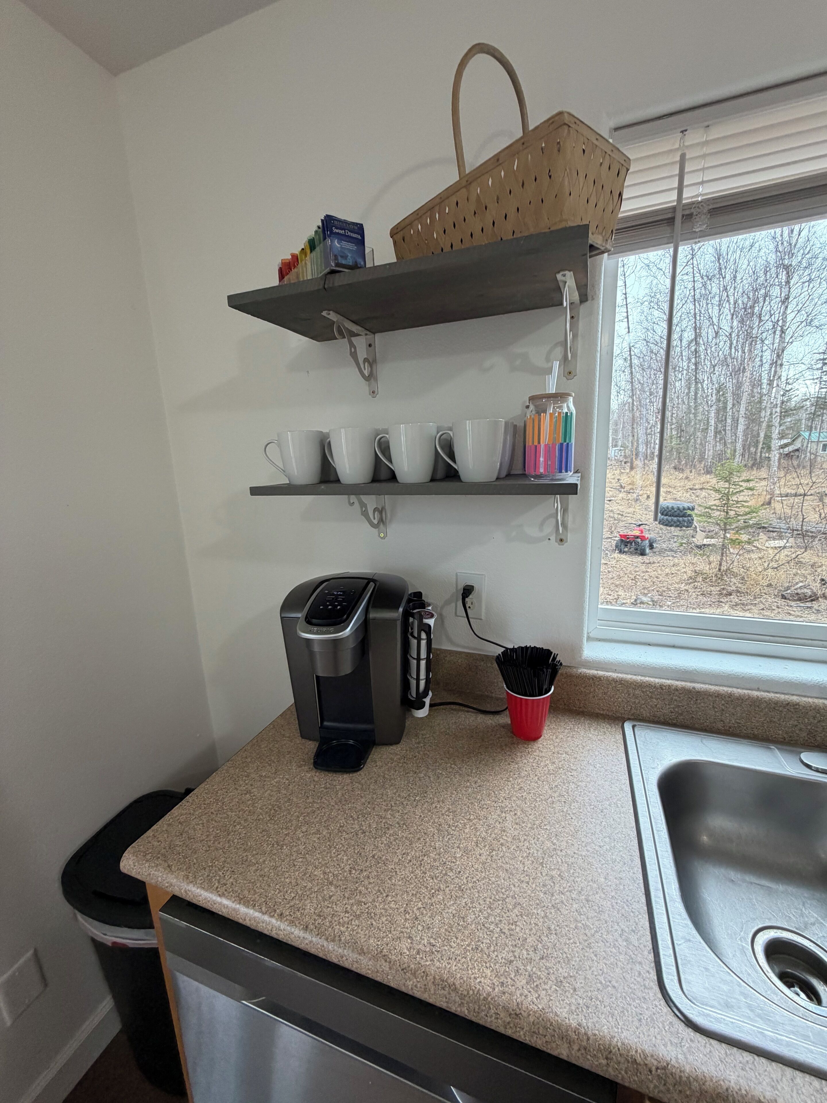 Une cuisine équipée d’une machine à café, d’un panier et de tasses rangées sur des étagères.