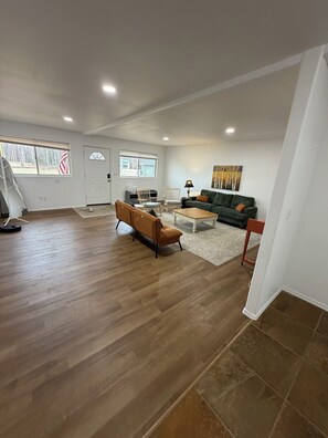 A spacious living area with hardwood flooring, a green sofa, a brown armchair, and a coffee table. -  3-bedroom house in charming Wasilla perfect for a family getaway (Wasilla)