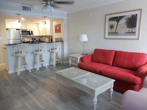 A compact living space with a kitchenette, a red sofa, a white coffee table, and a framed picture on the wall. - PARADISE FOUND! Beautiful Waterfront Escape with Marina View, 3rd Floor, 1 (Punta Gorda)