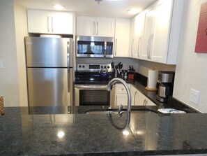 A kitchen with stainless steel appliances, white cabinets, a black countertop, and a stainless steel sink. - PARADISE FOUND! Beautiful Waterfront Escape with Marina View, 3rd Floor, 1 (Punta Gorda)