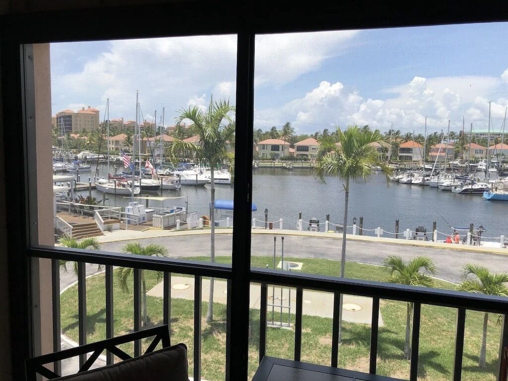 A marina view from a balcony with boats, palm trees, and buildings in the background.