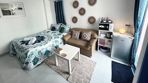 A bedroom with a bed, a sofa, a small table, a desk, a refrigerator, and a wall with decorative plates. - 401 Budget Room Utilities Wifi Balcony in Ratchada (Bangkok)