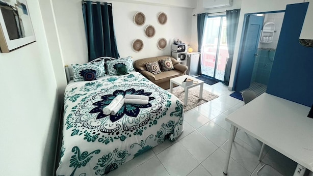 A bedroom with a bed, a sofa, a small table, a desk, and a bathroom with a shower. - 401 Budget Room Utilities Wifi Balcony in Ratchada (Bangkok)
