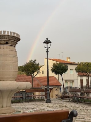 Una fuente de piedra, un farol y un edificio con techo de tejas rojas.