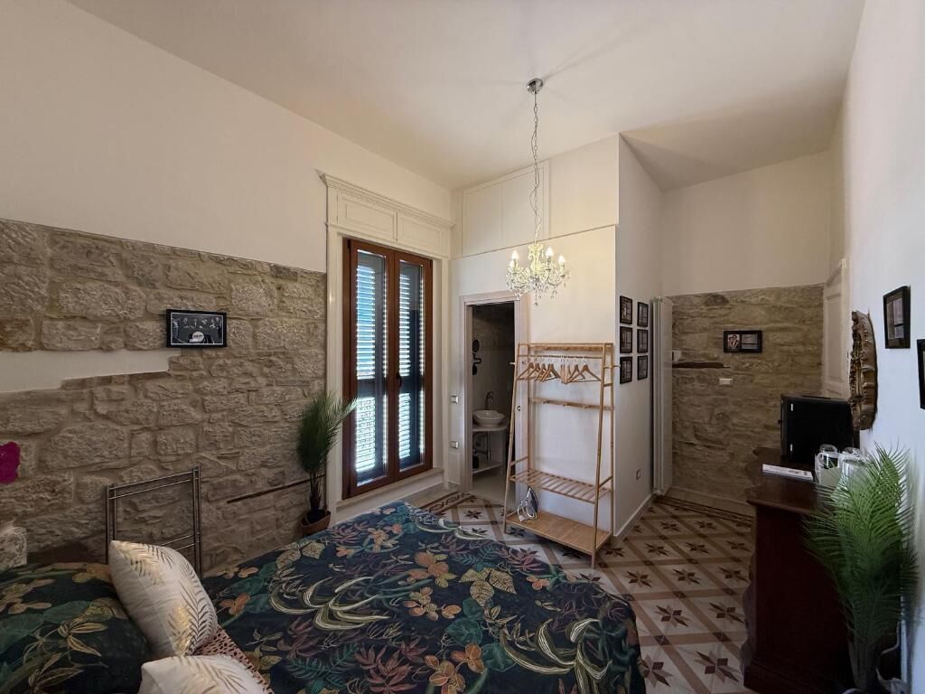 A room with a bed, a chandelier, a stone wall, and a door leading to a bathroom.