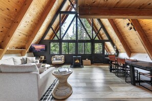 Een zolderkamer met een open haard, houten balken, een bank, een eettafel en stoelen.