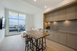 A modern kitchen with a large window, a wooden dining table, and a view of the cityscape.