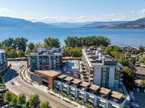 A modern building with multiple floors, a rooftop pool, and a view of a lake. - Lakefront Penthouse w/ Pool & Free EV Charging (Kelowna)
